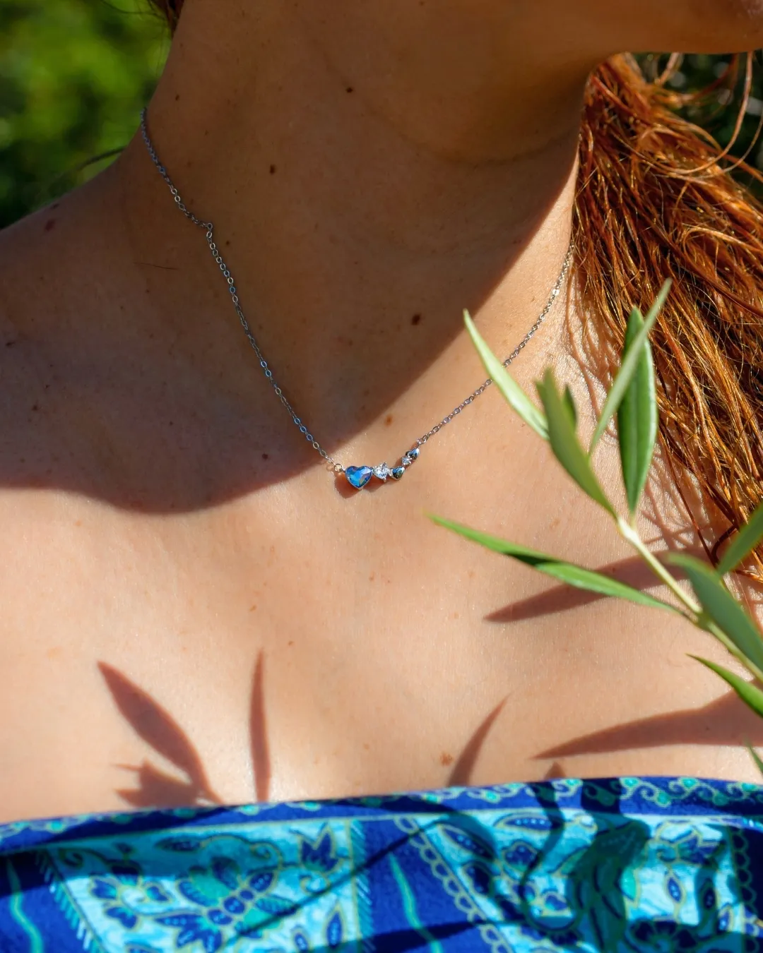 Srebrna ogrlica Diamond Glow Blue Heart na vratu modela, letnji kadar sa maslinovom grančicom