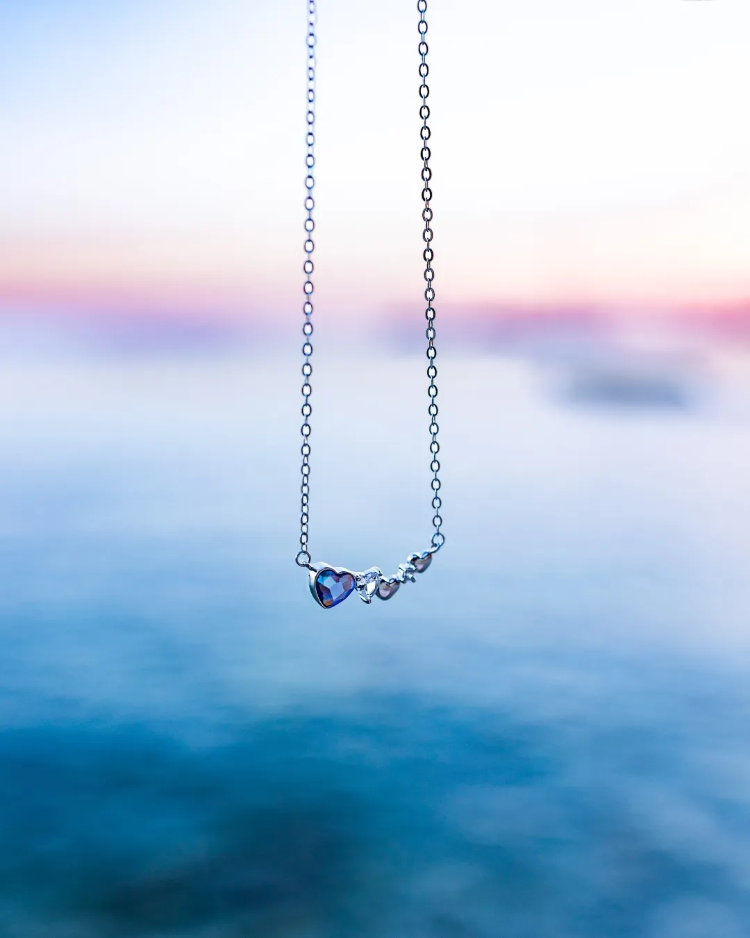 Srebrna ogrlica Diamond Glow Blue Heart sa plavim kristalnim srcem, obešena iznad mora u suton