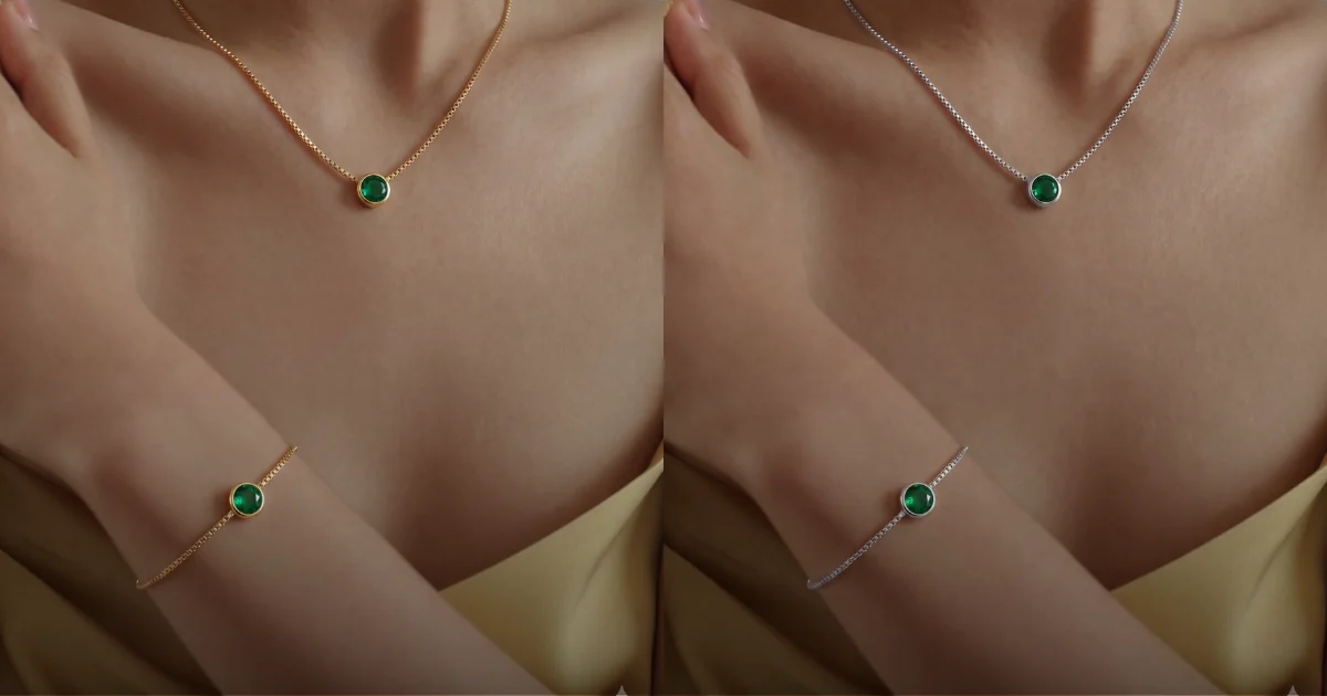 Diamond Glow Verde — zlatna ogrlica i narukvica sa smaragdnim kamenom, na šampanj pozadini