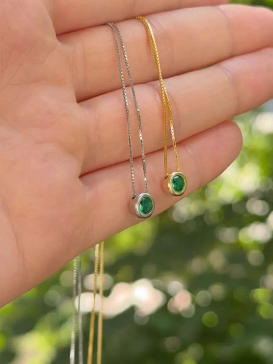 Ogrlice DG Verde Silver i DG Verde Gold sa zelenim kamenom na dlanu, napolju u zelenilu