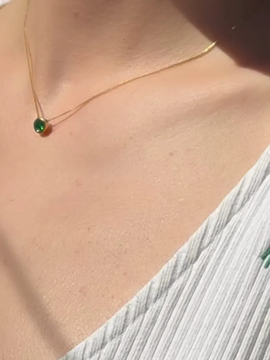 Pozlaćena ogrlica DG Verde Gold sa zelenim kamenom na vratu, uz belu majicu, na suncu
