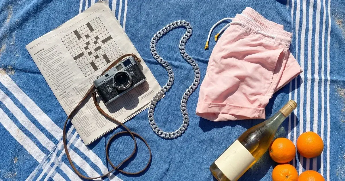 Srebrni Cuban Link lanac od 925 srebra na peškiru za plažu, pored fotoaparata, novina i letnjih sitnica — nakit na letovanju.
