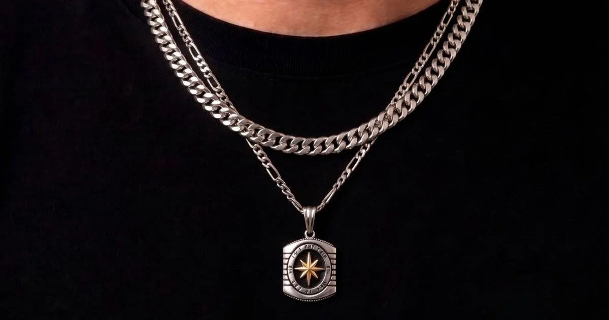 Muška srebrna ogrlica Figaro Light sa priveskom na dužem lancu uz čistu Cuban Link ogrlicu pri vratu — layering muškog nakita od 925 srebra.