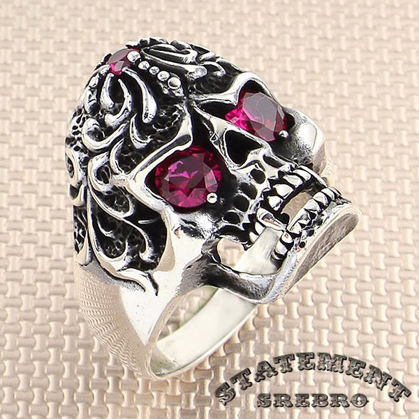 Muški prsten od 925 Srebra u obliku kosturske glave sa gravurom i crveno-rozim kamenjem, pokazuju pravi sklop lepog i opasnog.