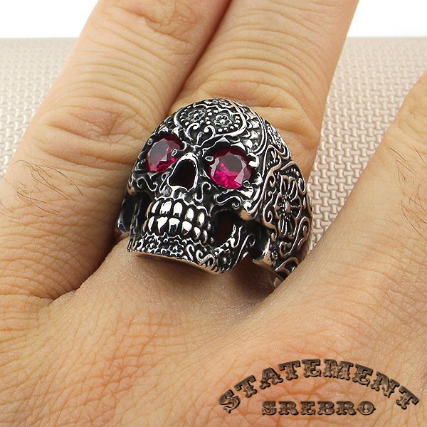 Muški prsten od 925 Srebra u obliku kosturske glave sa gravurom cveta i crveno-rozim kamenom, pokazuju pravi sklop lepog i opasnog.
