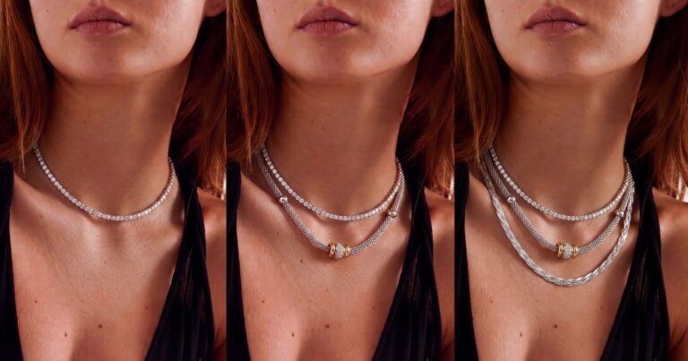 Žena nosi tri srebrne ogrlice različitih dužina preko bele košulje, prikazujući layering trend.